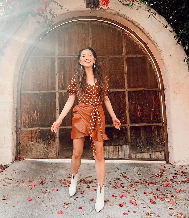 Jenn Im, una de las youtubers de moda que más dinero gana, posando vestida con un conjunto de top marrón con topos blancos, una falda marrón de tiro alto y unas botas blancas.