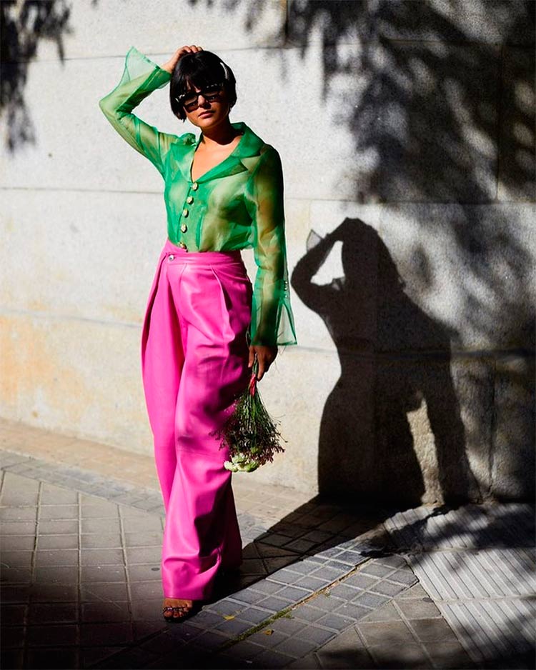 La diseñadora María Bernad posa con un conjunto elegante formado por una pantalón bombacho fucsia y una blusa de organza transparente verde, unas sandalias y un ramo de flores, un outfit tendencia 2020 con una prenda imprescindible en tu armario.