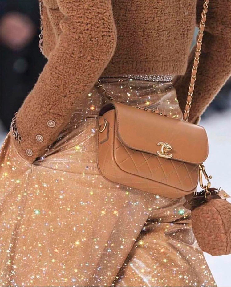 Un bolso mini nude de Chanel colgado del hombro de una modelo en una pasarela, no olvides comprar bolsos rebajas.
