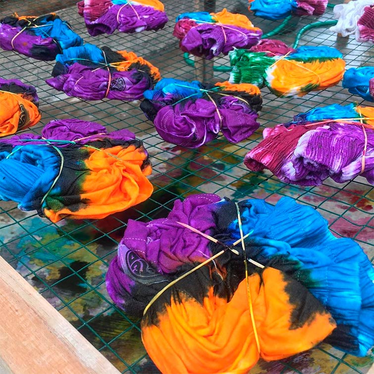 Aparecen unas camisetas tie dye en el proceso de teñirse, enroscadas y llenas de las tintas de colores, así es la forma de hacer la ropa tie-dye.