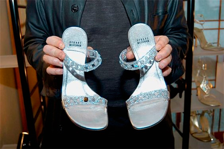 Aparecen las Cinderella slippers sujetas por las manos de un hombre y se aprecian los diamantes y por qué son unos de los zapatos mujer más caros del mundo.