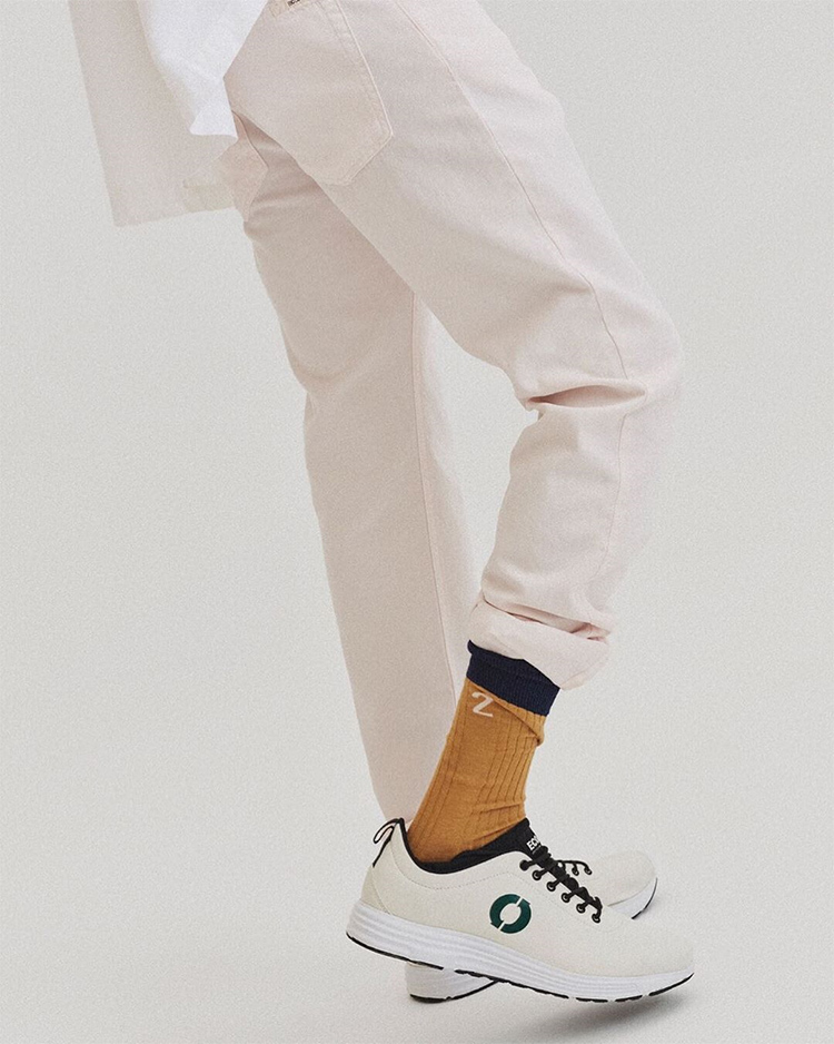Una persona posa con unas zapatillas veganas blancas y pantalones blancos.
