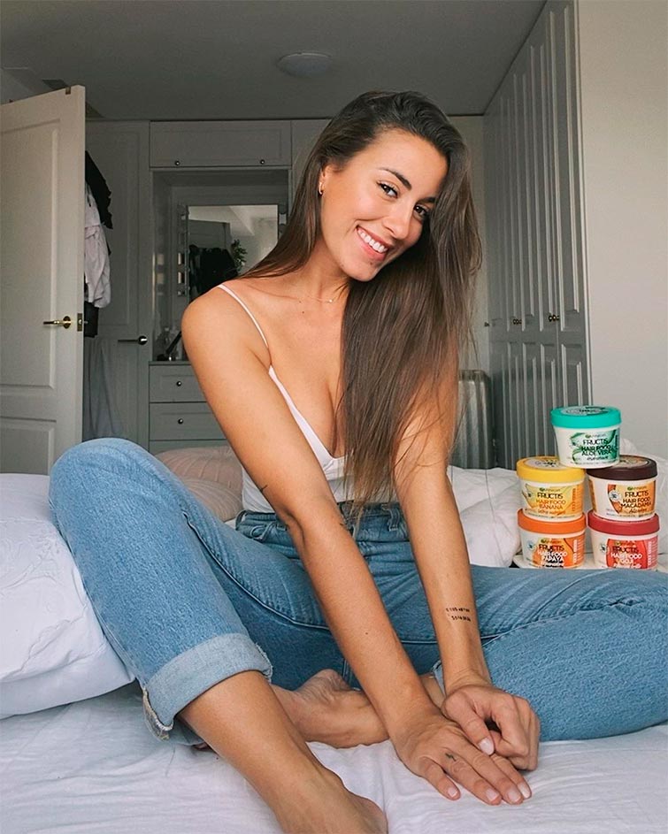 Paula Gonu en uno de sus post de Instagram publicitando unos productos para el pelo en actitud desenfadada, con unos jeans y una básica blanca.