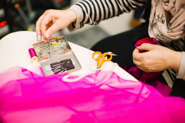 Manos de una trabajadora cosiendo ropa slow fashion movement con tela rosa.