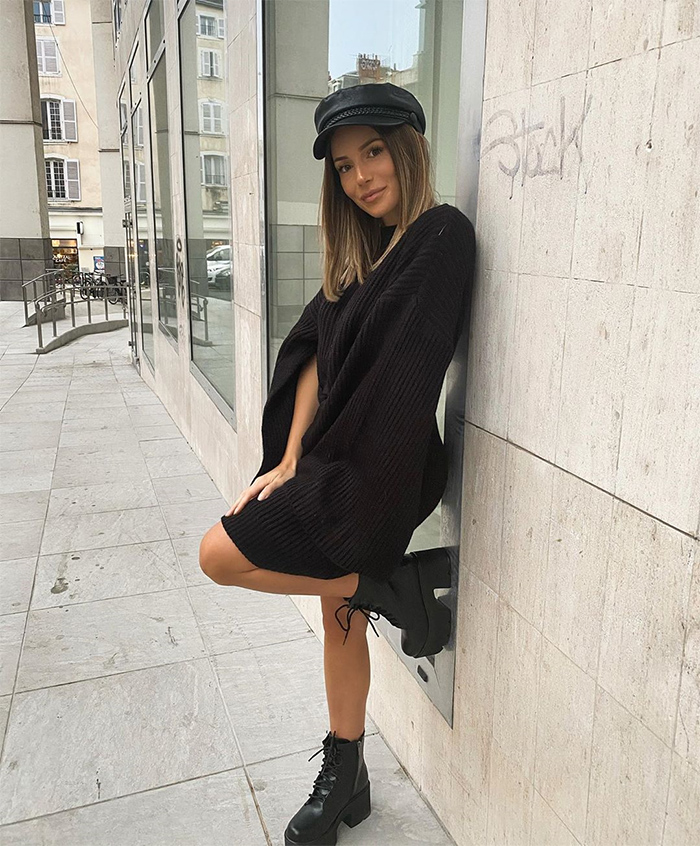 Chloe Fit vestida entera de negro, con botas de plataforma y gorra, usando truco moda parecer delgada, posando en la calle.