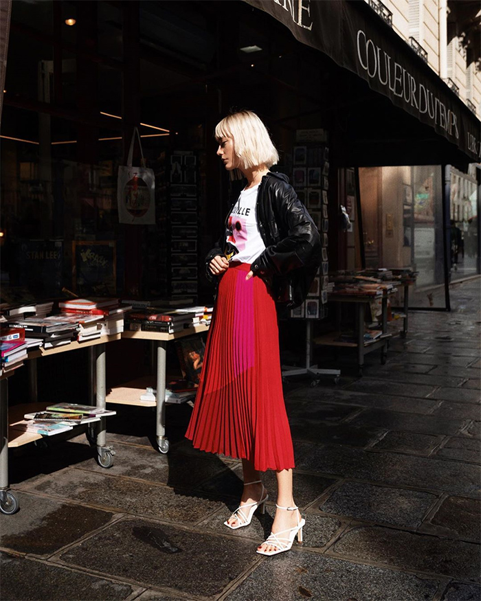 Marie Gilliot vestida con camiseta blanca, falda larga roja y chaqueta negra, posando en la calle, usando truco moda parecer delgada.
