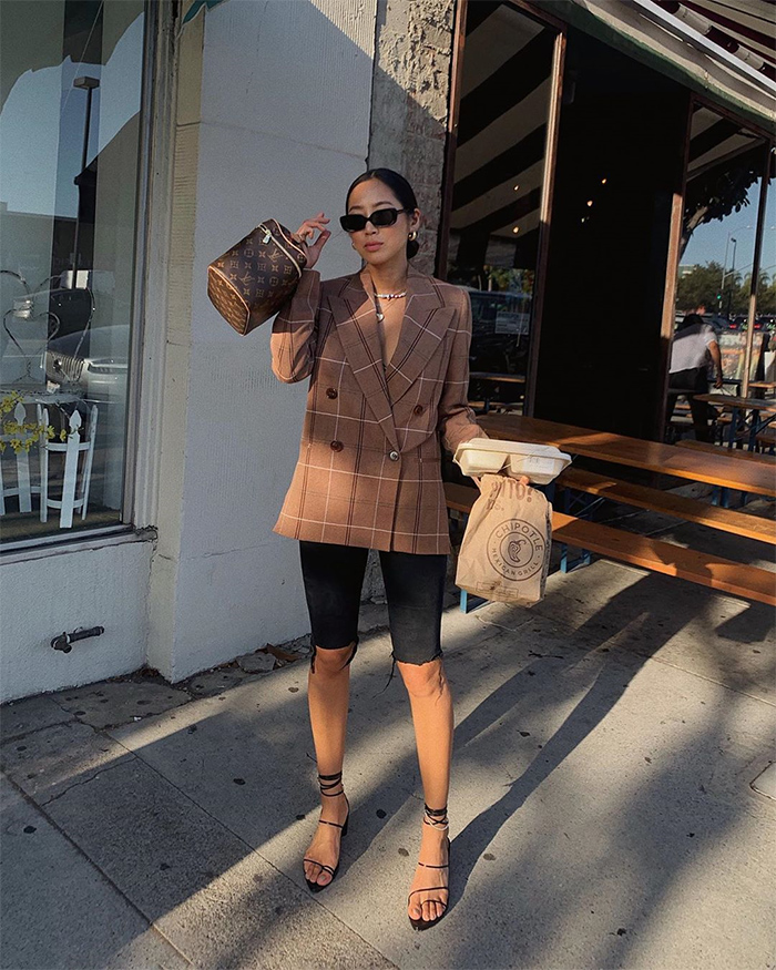 Aimee Song posando con chaqueta marrón, pantalones piratas negros y gafas de sol, posando en la calle, usando truco moda parecer delgada.
