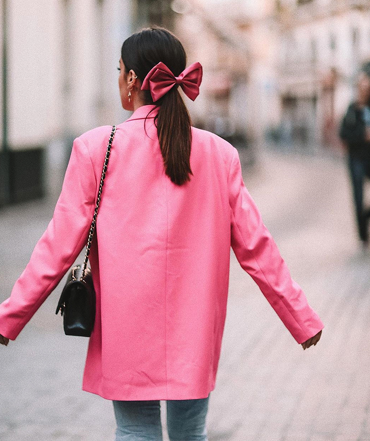 Dulceida lleva una blazer rosa combinada con unos pantalones anchos vaqueros, un bolso negro mini y un lazo fucsia en la coleta, el mejor look San Valentín. 