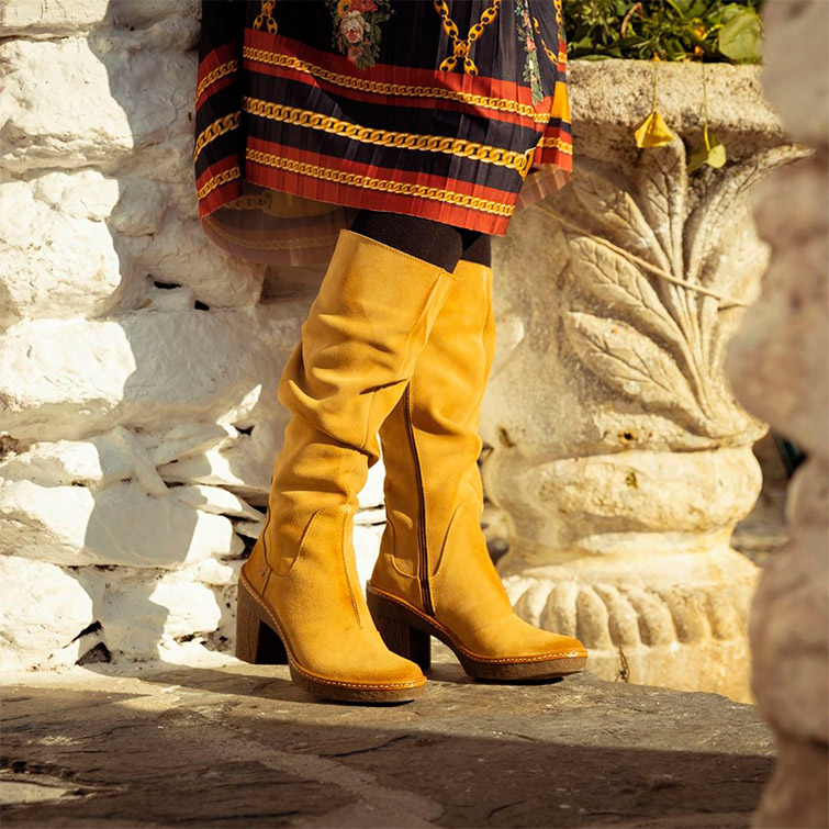 Mujer posando con una falda étnica de color negro y naranja y botas de tacón amarillas, vestida con las prendas de una de las marcas de moda sostenible España.