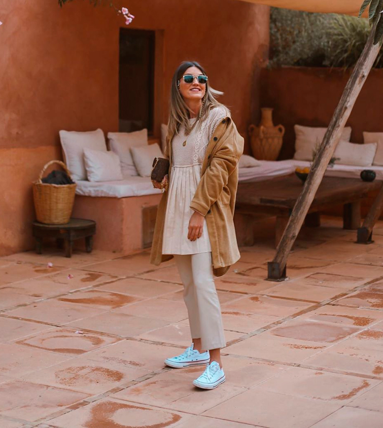 La influencer Cristina Cerqueiras viste un pantalón beige, blusa beige, chaqueta marrón camel combinado con unas zapatillas blancas Converse
