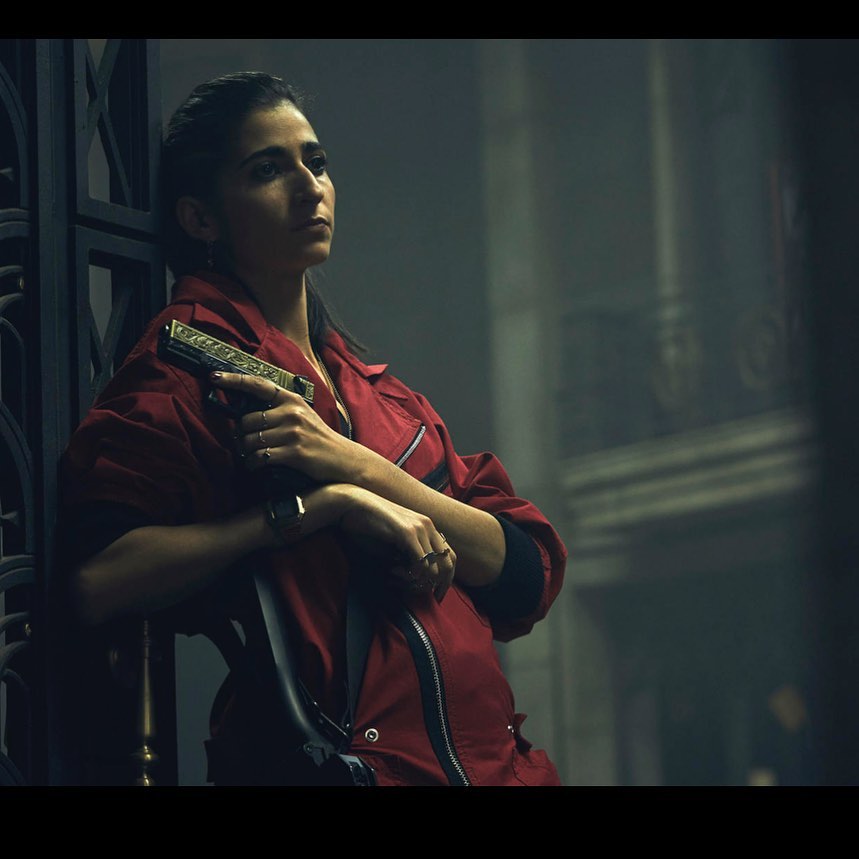 Alba Flores en una secuencia de la serie la Casa de Papel de Netflix en la que protagoniza a Nairobi, vestido con el famoso buzo rojo y con una pistola en la mano.

