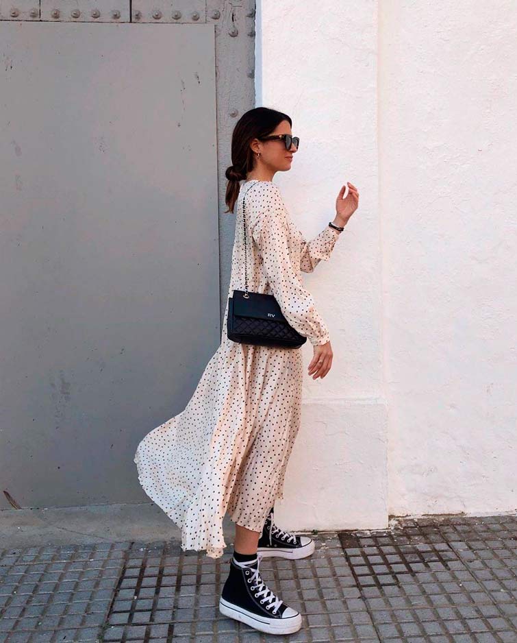 Maria Valdes viste un vestido largo verano de lunares combinado con unas zapatillas Converse negras de bota y plataforma y un elegante bolso negro
