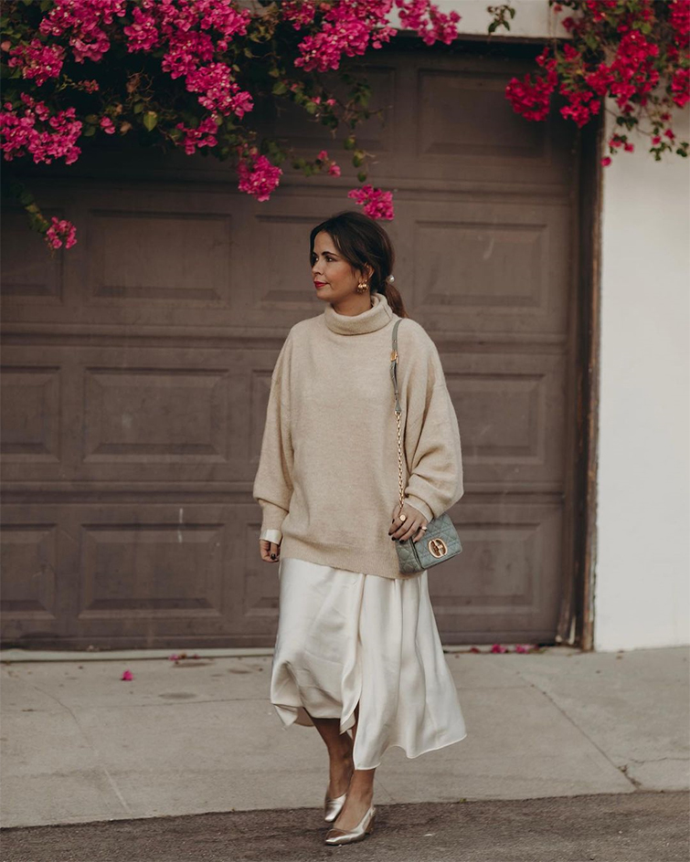 Sara Escudero, conocida blogger de moda como collagevintage, camina por la calle vestida con un jersey beige de cuello alto, y una maxifalda blanca