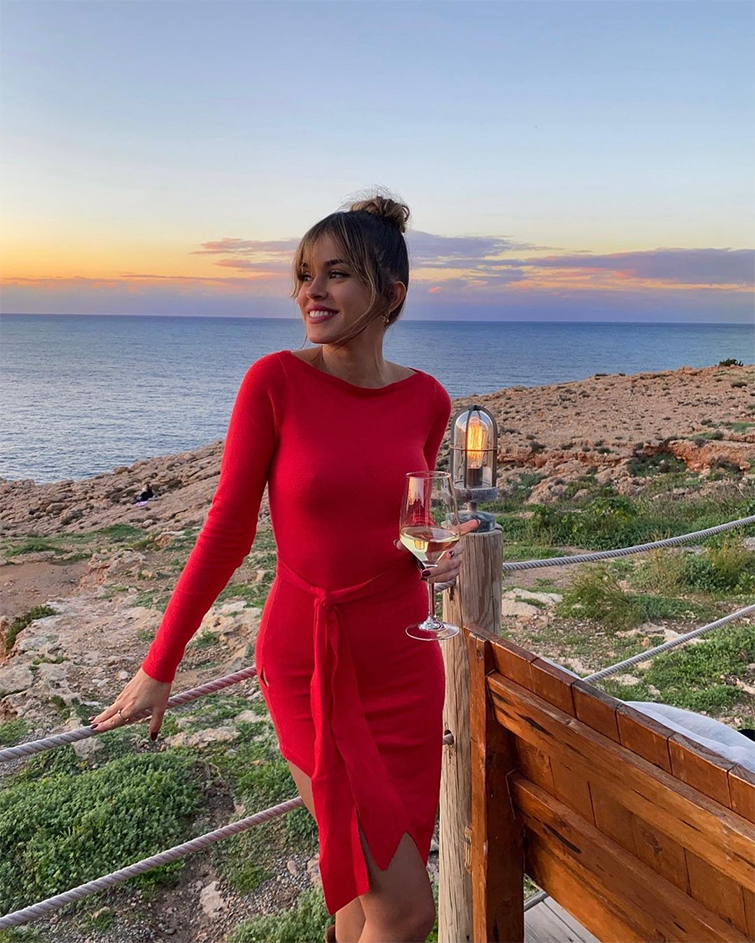 Rocio Camacho se ha convertido en poco tiempo en una de las instagramers de moda más importantes. En la foto posa en un atardercer frente a la costa con un vestido rojo midi y una copa de champagne en la mano