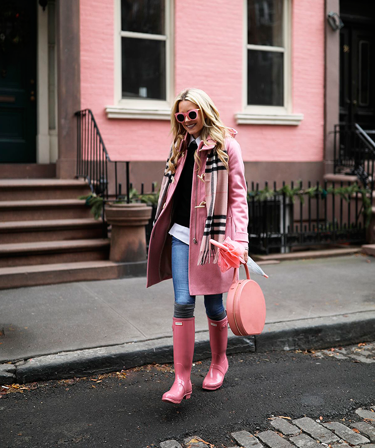 Mujer rubia de pelo largo camina por la calle, ella es la bloguera Blaireadiebee y lleva un outfit botas hunter mujer totalmente rosa