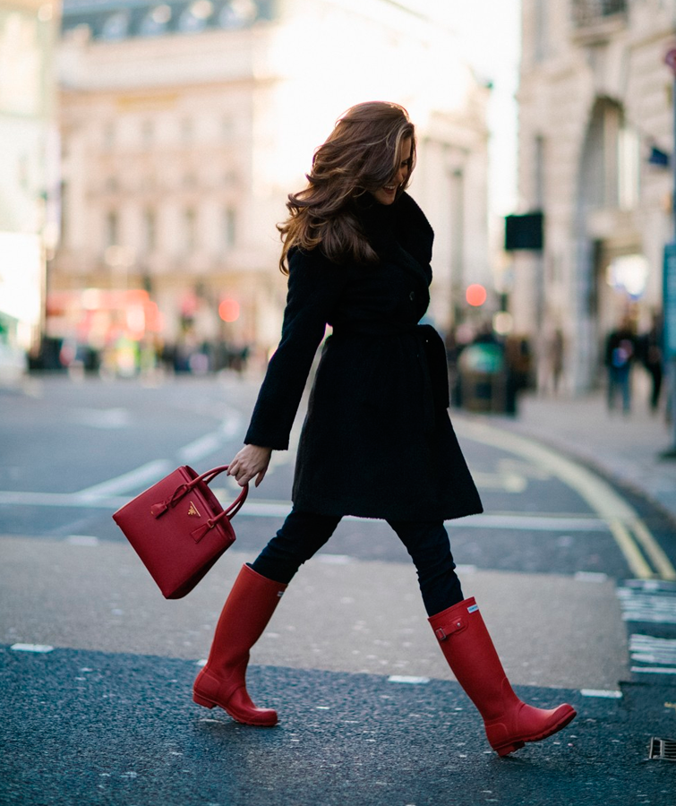 La bloguera Rosielondoner camina vestida de negro con unas botas de agua rojas, ella sabe Cómo combinar botas Hunter de mujer de segunda mano