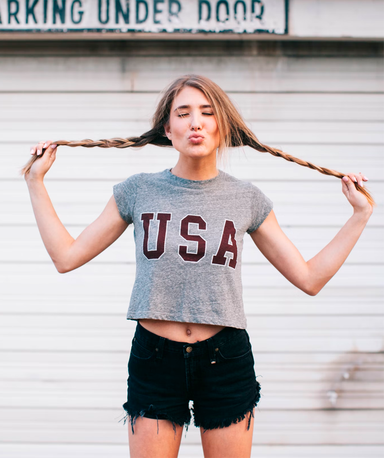 Imagen de chica que lleva ropa americana mujer, pantalones vaqueros cortos negros y una camiseta gris con un mensaje que dice "USA".